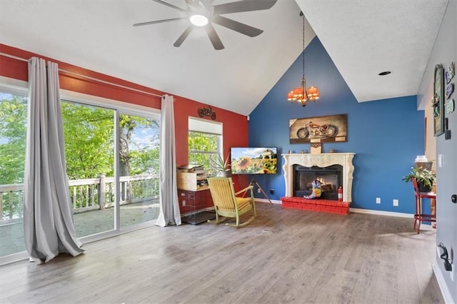 sitting room featuring wood finished floors, baseboards, high vaulted ceiling, a fireplace with raised hearth, and ceiling fan with notable chandelier