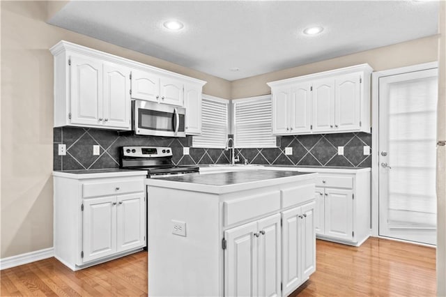 18461 W 157th St, Olathe, KS 66062 - kitchen featuring appliances with stainless steel finishes, white cabinetry, light wood finished floors, a kitchen island, and backsplash