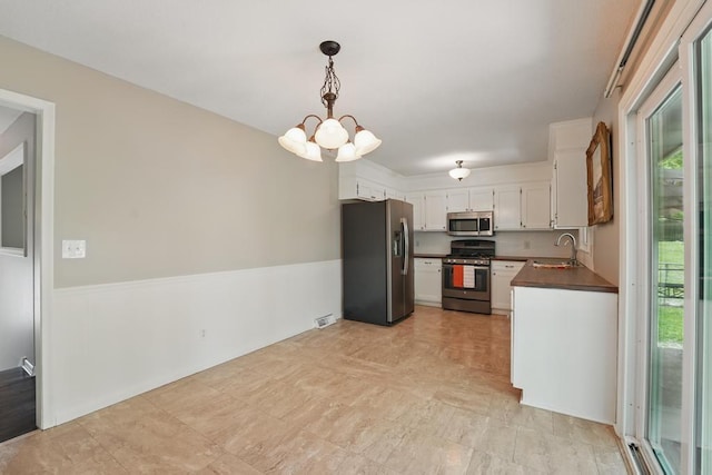 8020 Yecker Ave, Kansas City, KS 66109 - kitchen with appliances with stainless steel finishes, dark countertops, a chandelier, white cabinetry, and a wainscoted wall