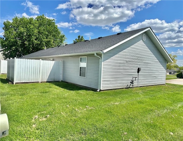 view of home's exterior featuring fence, a shingled roof, and a lawn