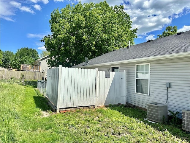 exterior space with a lawn, central air condition unit, roof with shingles, and fence