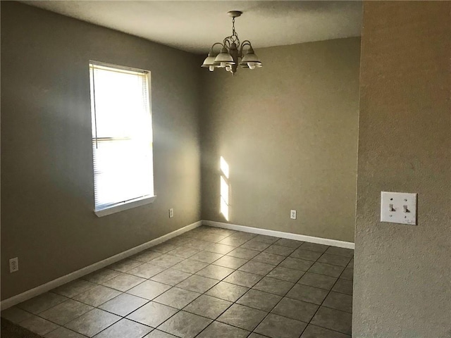 empty room featuring tile patterned floors, a wealth of natural light, baseboards, and a notable chandelier