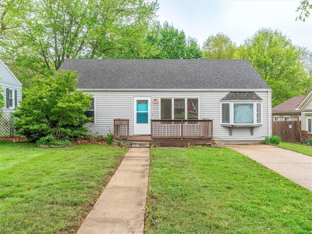 view of front of home featuring a deck, roof with shingles, a front lawn, and fence