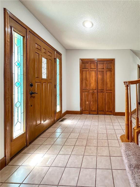 entrance foyer with a textured ceiling, stairs, baseboards, and light tile patterned flooring
