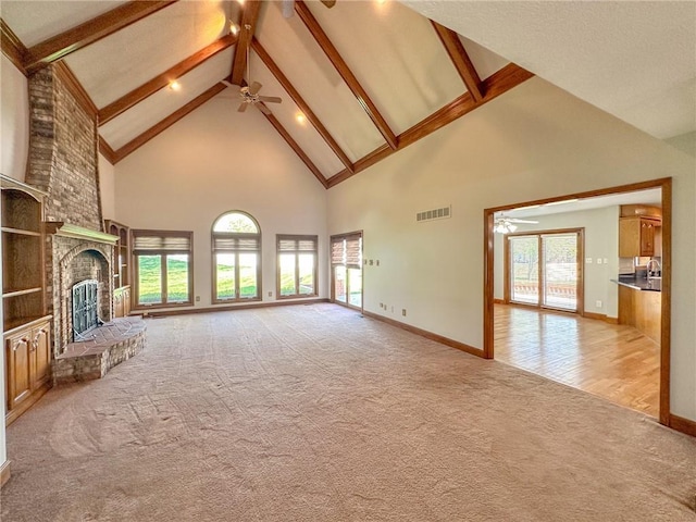 unfurnished living room featuring ceiling fan, high vaulted ceiling, light colored carpet, healthy amount of natural light, and beamed ceiling