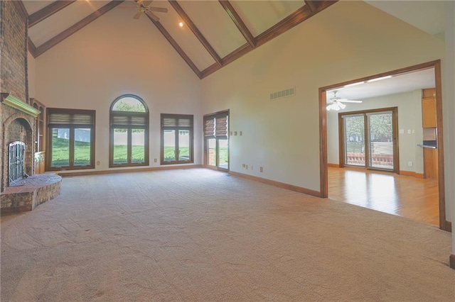 unfurnished living room with a ceiling fan, high vaulted ceiling, a fireplace, beamed ceiling, and light carpet