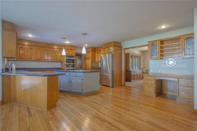 kitchen with appliances with stainless steel finishes, a sink, light wood finished floors, dark countertops, and decorative light fixtures