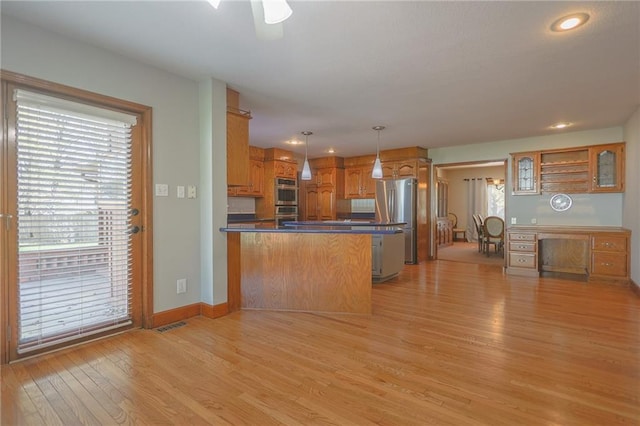 kitchen featuring stainless steel appliances, a peninsula, dark countertops, light wood-style floors, and pendant lighting