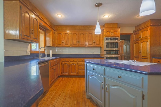 kitchen with a sink, stainless steel appliances, dark countertops, brown cabinetry, and recessed lighting