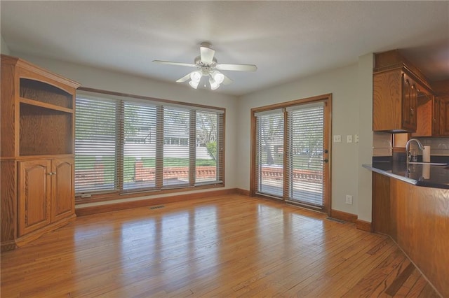 unfurnished living room featuring a sink, ceiling fan, light wood-style floors, and baseboards
