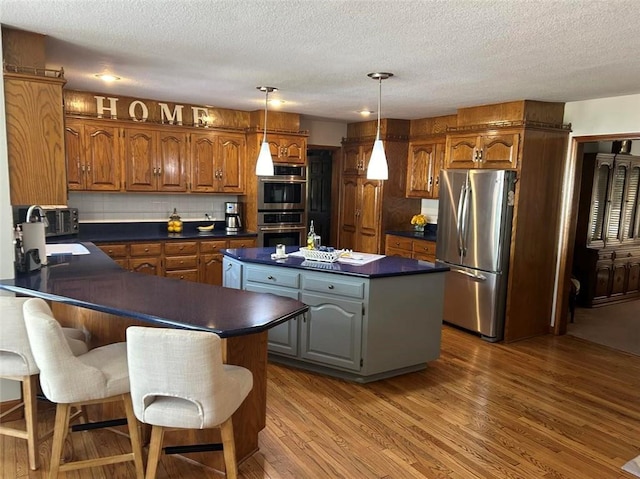 kitchen with stainless steel appliances, dark countertops, a kitchen island, wood finished floors, and a peninsula