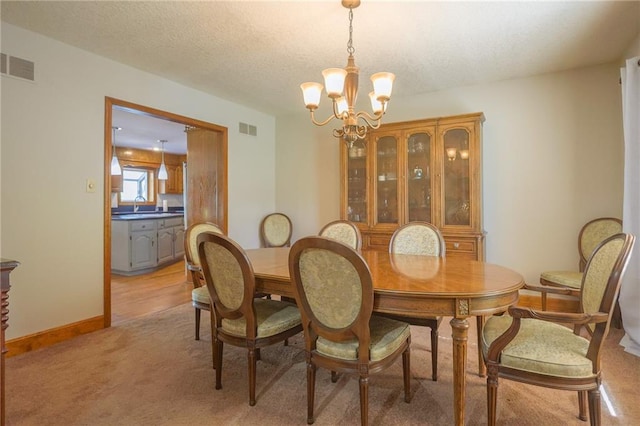 dining space with a chandelier, light colored carpet, a textured ceiling, and baseboards