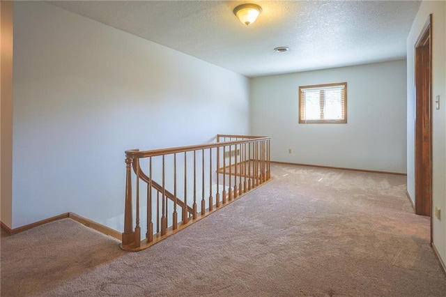 hallway featuring an upstairs landing, carpet floors, baseboards, and a textured ceiling