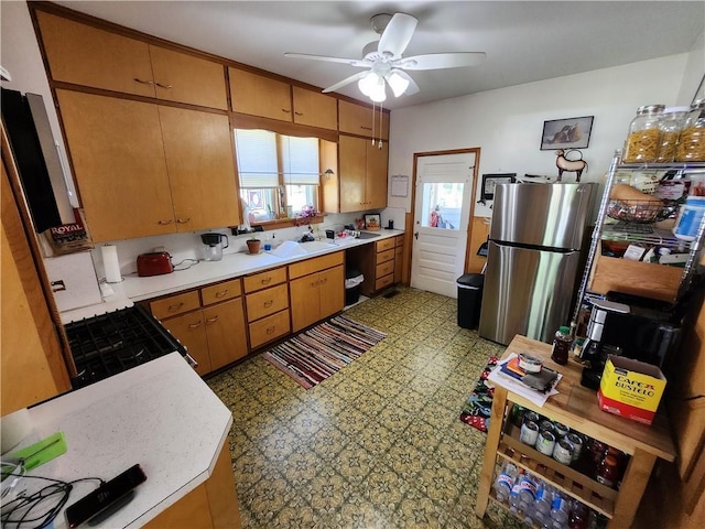 kitchen featuring freestanding refrigerator, light floors, gas range, ceiling fan, and light countertops