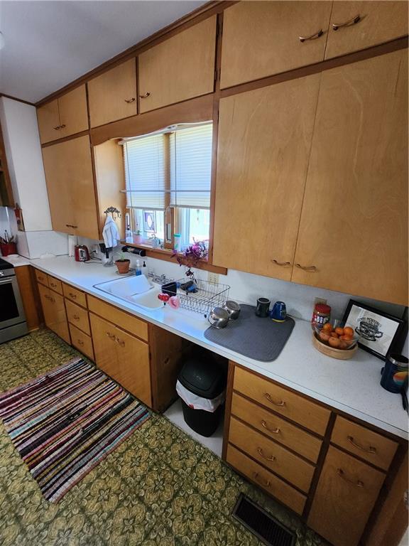kitchen featuring visible vents, a sink, tile patterned floors, stainless steel range with electric stovetop, and light countertops