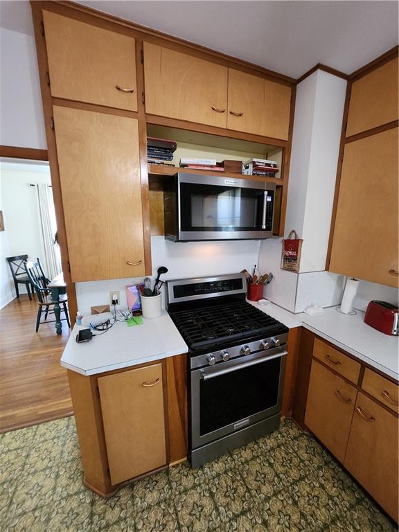 kitchen with light countertops, stainless steel appliances, dark floors, and brown cabinetry