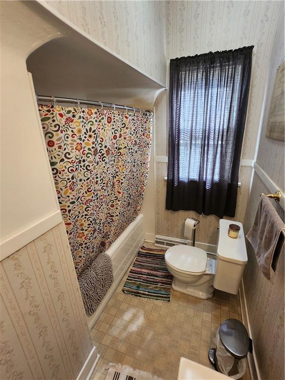 bathroom featuring shower / bath combination with curtain, toilet, and wallpapered walls