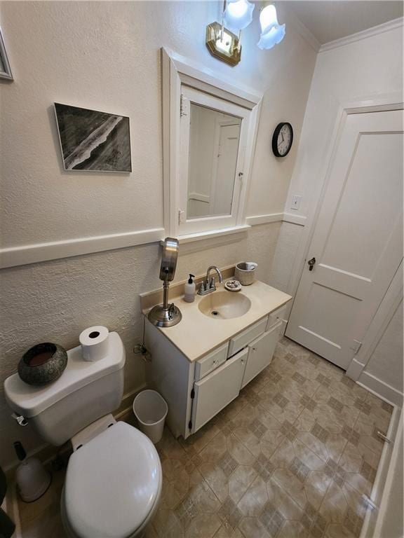 half bath featuring toilet, tile patterned floors, crown molding, a textured wall, and vanity