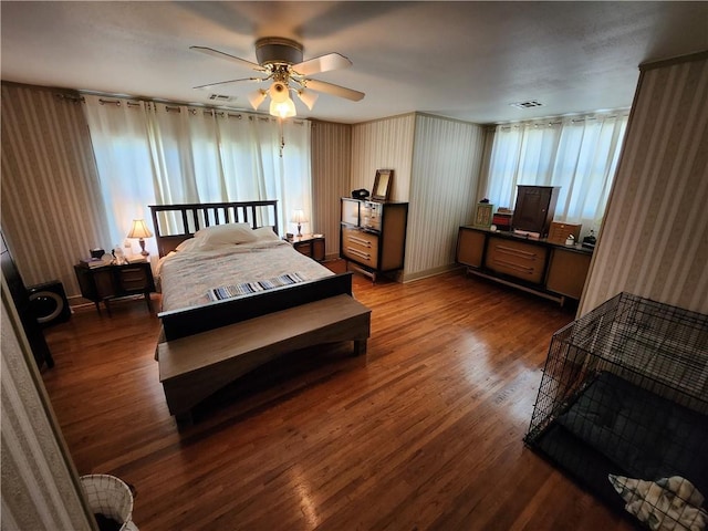 bedroom with wallpapered walls, dark wood finished floors, visible vents, and a ceiling fan