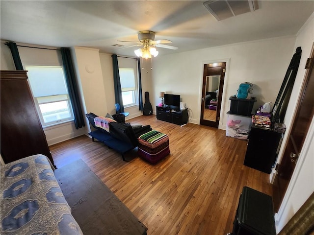 living room featuring visible vents, crown molding, wood-type flooring, a ceiling fan, and baseboards