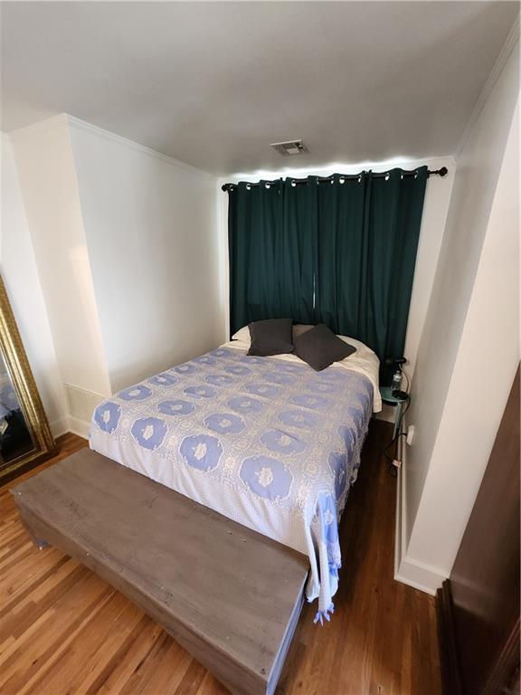 bedroom with ornamental molding, baseboards, visible vents, and wood finished floors