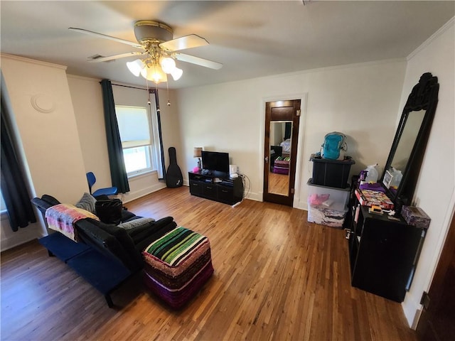 living area featuring ceiling fan, crown molding, baseboards, and wood finished floors