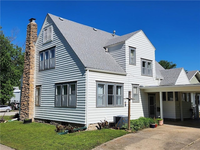 cape cod home with a shingled roof, an attached carport, a chimney, and driveway