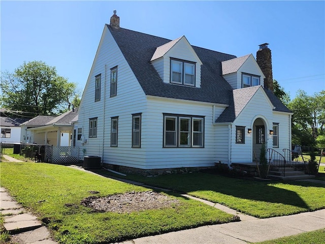 cape cod-style house featuring roof with shingles, a chimney, and a front yard