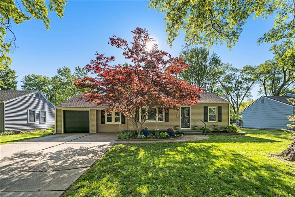 view of property hidden behind natural elements with an attached garage, a front lawn, and driveway