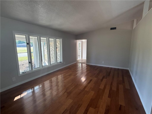 empty room featuring a textured ceiling, visible vents, wood finished floors, and baseboards