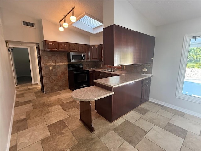 kitchen with lofted ceiling with skylight, a sink, stainless steel microwave, a peninsula, and electric range