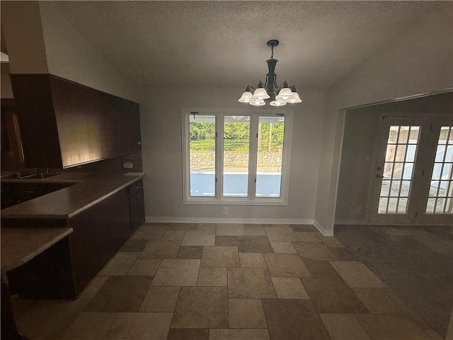 unfurnished dining area with stone finish flooring, a textured ceiling, baseboards, a chandelier, and lofted ceiling