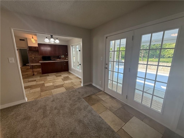 entryway featuring a textured ceiling, visible vents, an inviting chandelier, stone finish flooring, and baseboards