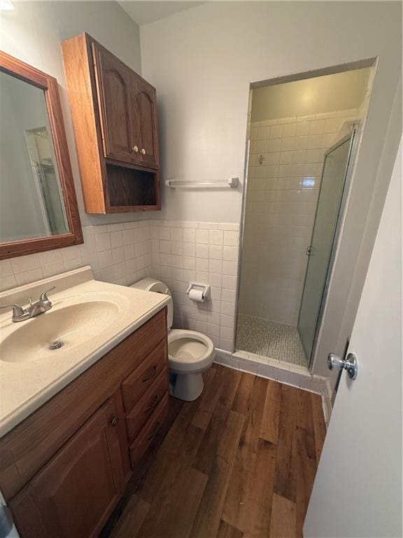 bathroom featuring a stall shower, tile walls, toilet, vanity, and wood finished floors