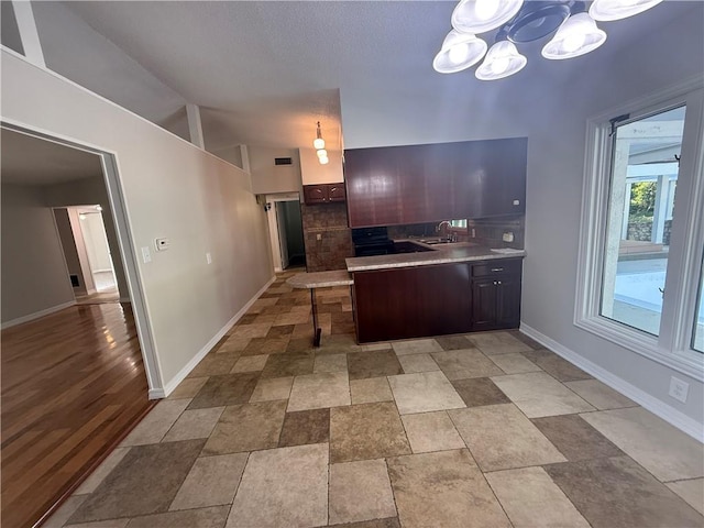 kitchen with a peninsula, a sink, a notable chandelier, baseboards, and backsplash