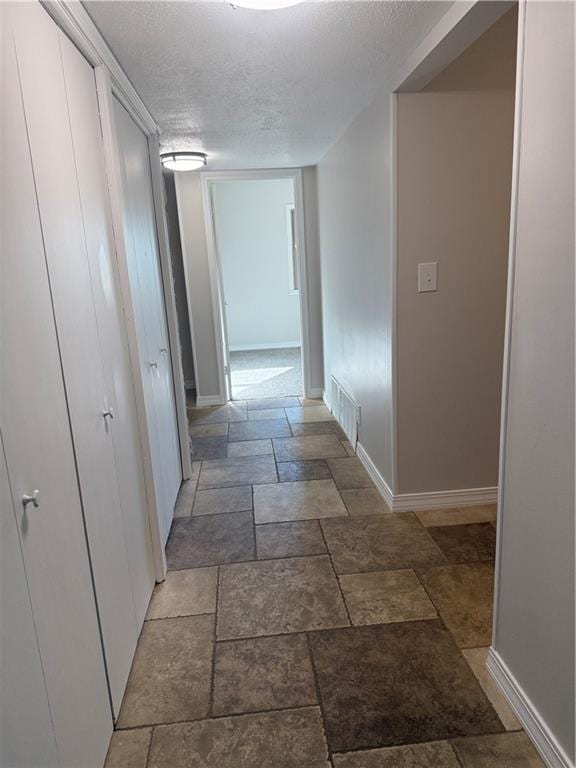hallway featuring a textured ceiling, visible vents, baseboards, and stone tile floors