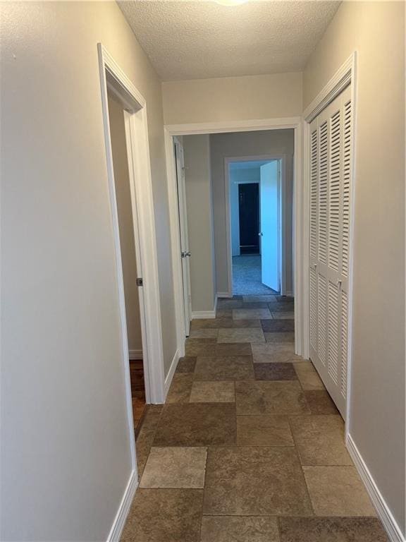 corridor featuring a textured ceiling and baseboards