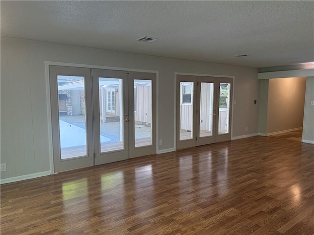 interior space with a textured ceiling, visible vents, french doors, and wood finished floors
