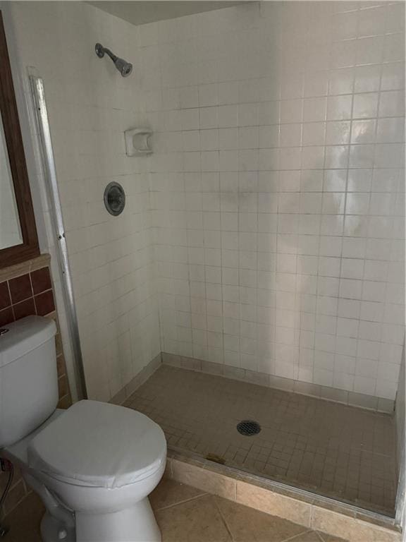 bathroom featuring tile patterned flooring, toilet, tile walls, and a shower stall