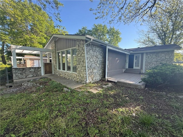 rear view of property with fence, stone siding, and a deck