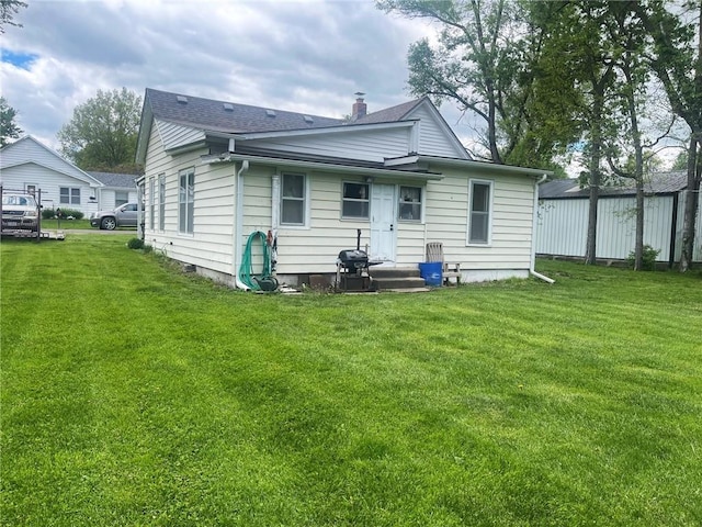 back of house with a yard, a shingled roof, and a chimney