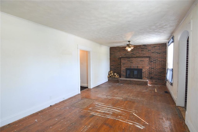 1221 Morgan Ave, Parsons, KS 67357 - unfurnished living room with hardwood / wood-style floors, a textured ceiling, a brick fireplace, a ceiling fan, and baseboards