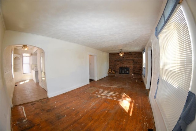 1221 Morgan Ave, Parsons, KS 67357 - unfurnished living room featuring wood-type flooring, a brick fireplace, a ceiling fan, and arched walkways
