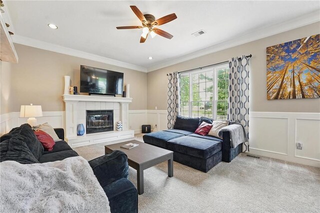 living area featuring crown molding, a ceiling fan, light colored carpet, a decorative wall, and wainscoting