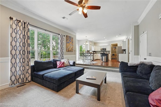 carpeted living area with a ceiling fan, a wainscoted wall, crown molding, and a decorative wall