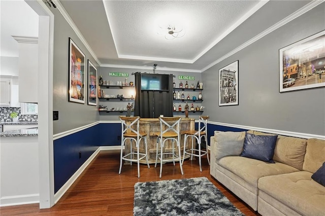 indoor dry bar with a raised ceiling, wood finished floors, decorative backsplash, ornamental molding, and baseboards