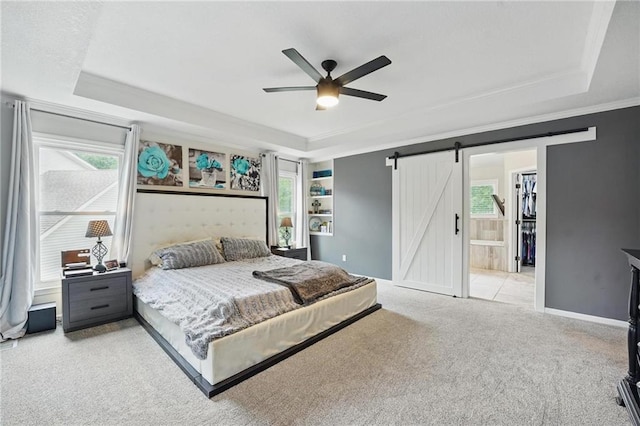 bedroom featuring a tray ceiling, a barn door, carpet floors, crown molding, and ceiling fan