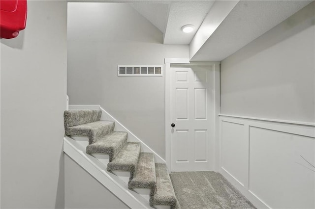 staircase featuring a decorative wall, a wainscoted wall, and carpet flooring