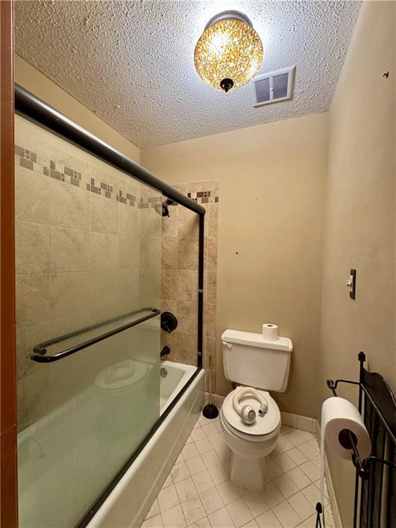5212 Somerset Dr, Prairie Village, KS 66207 - full bath with toilet, bath / shower combo with glass door, a textured ceiling, and tile patterned flooring