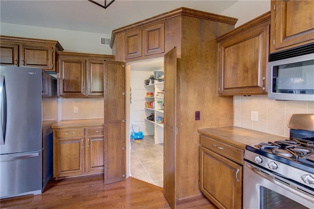 8812 NE 101st St, Kansas City, MO 64157 - kitchen featuring appliances with stainless steel finishes, decorative backsplash, brown cabinets, and wood finished floors